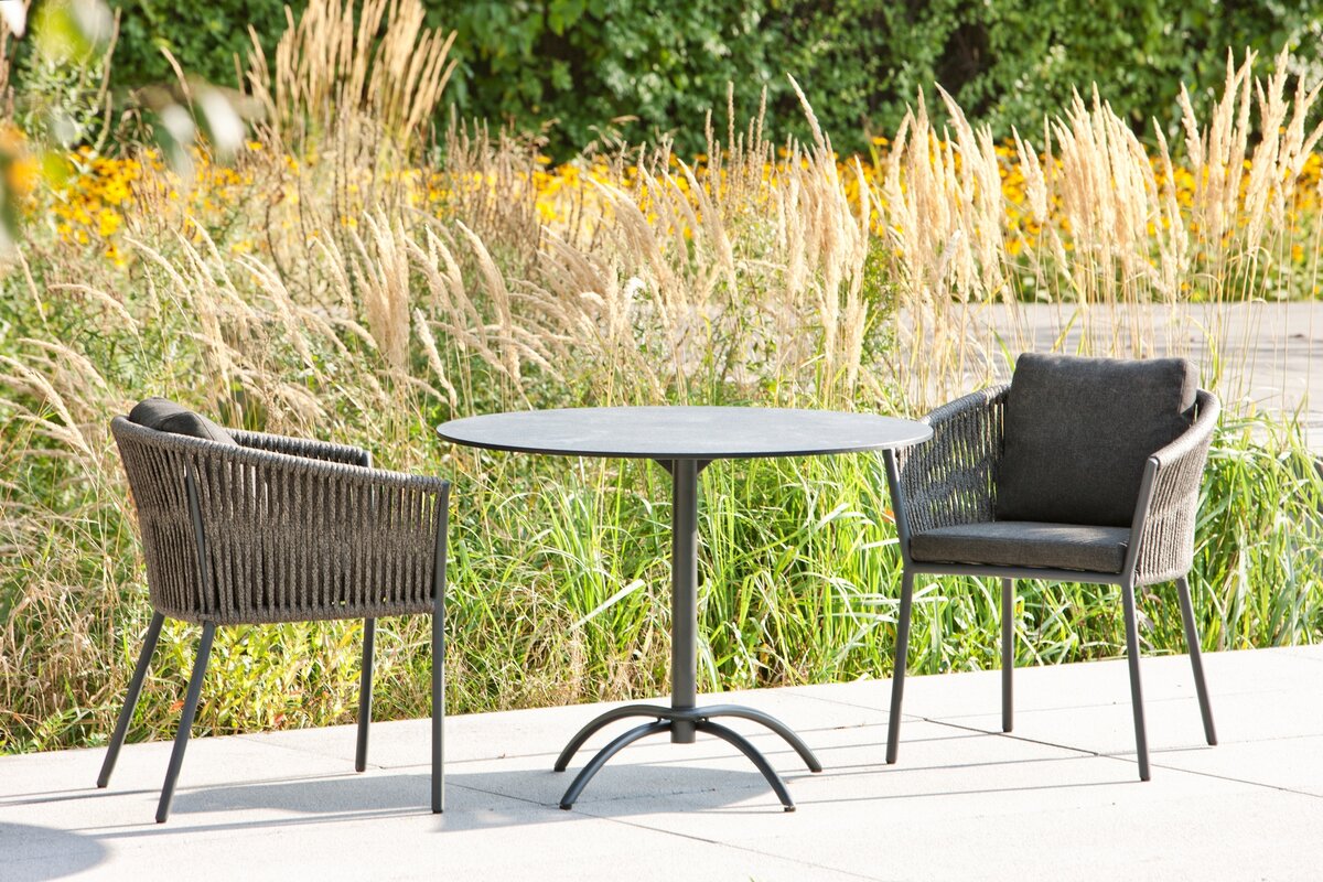 Gartentisch und Stühle auf Terrasse mit Gräsern und Blumen