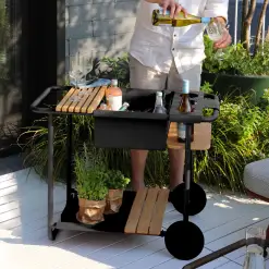 Mann schenkt Getränk aus Servierwagen auf sonniger Terrasse ein.